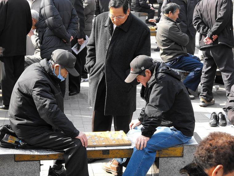 공원에서 마주 앉아 장기를 두는 어르신들과 둘러선 사람들